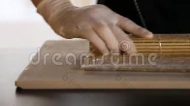 厨师的手在竹席上卷起寿司卷。寿司制作过程。把寿司卷卷起来